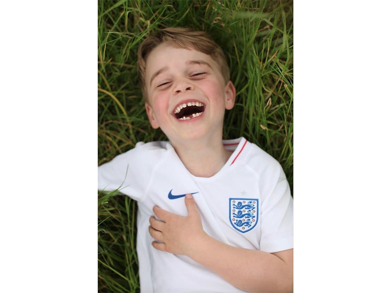 Prince George laughing in the grass in a soccer shirt