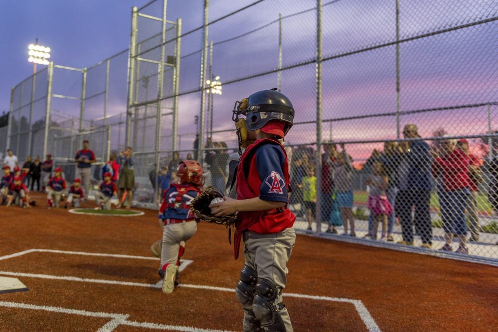 A kids' baseball game with a pink sunset in the background