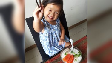 young girl eating bowl of noodles