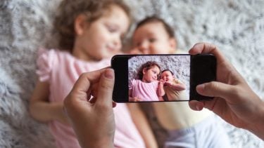 A mom takes a photo of her two kids with a phone