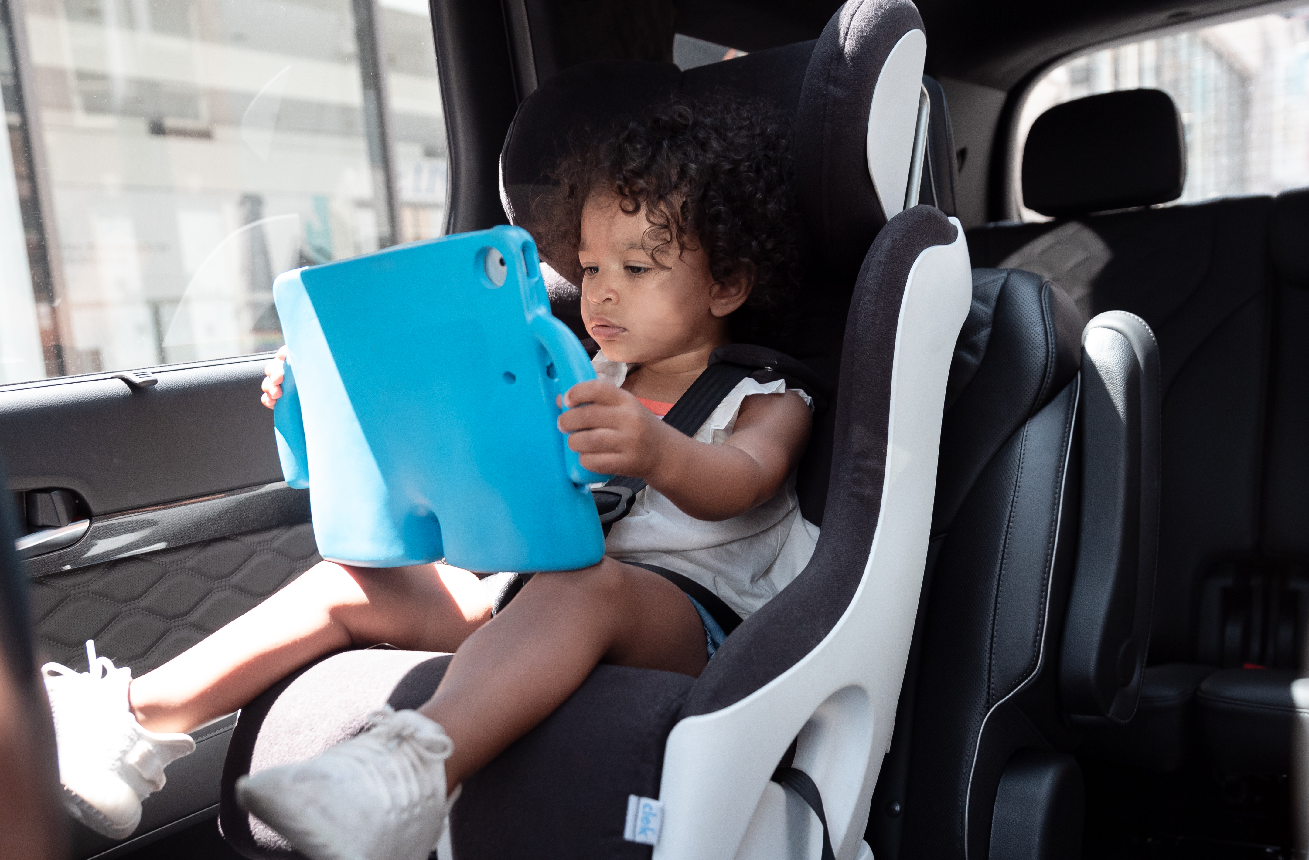 Sasha's toddler daughter in car seat holding an ipad