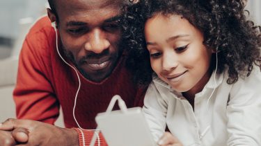 Dad and daughter look at phone with headphones