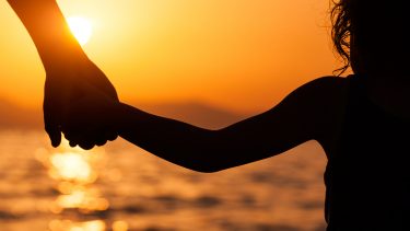 Woman and toddler holding hands at sunset