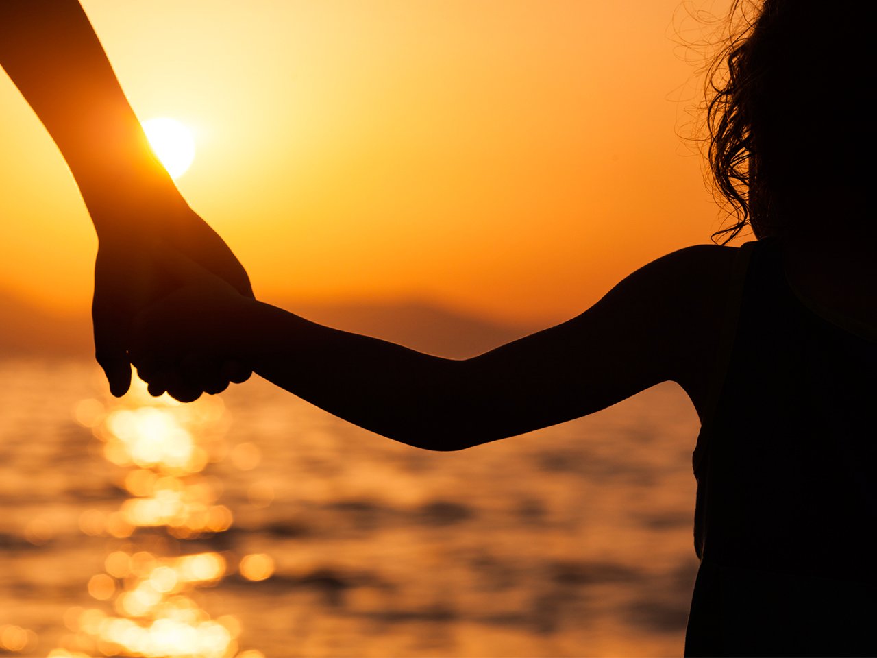  kvinna och småbarn håller händerna vid solnedgången