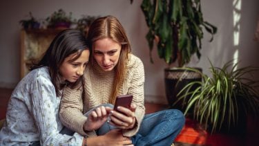 Mother and daughter look down at smartphone concerned