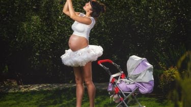 pregnant woman in a white tutu holding up a baby doll