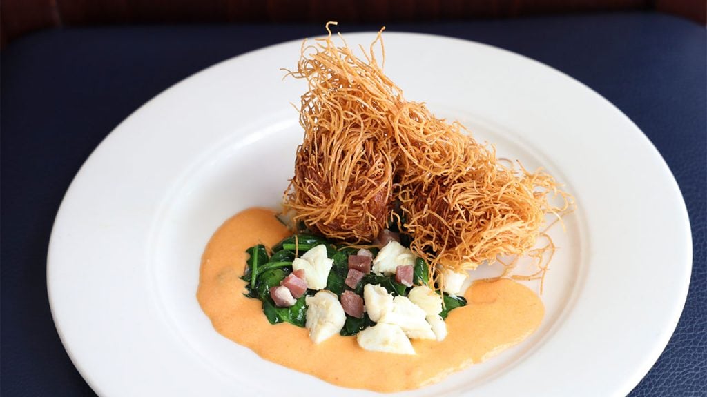 A plate of sea scallops rolled in shredded phyllo, fried crisp, and served on a bed of wilted spinach, lump crab and proscuitto ham with a shrimp cream sauce.