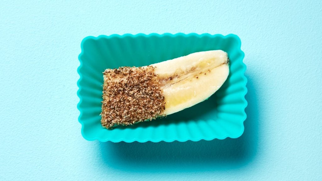 a piece of banana dipped in ground chia seeds in a teal cup