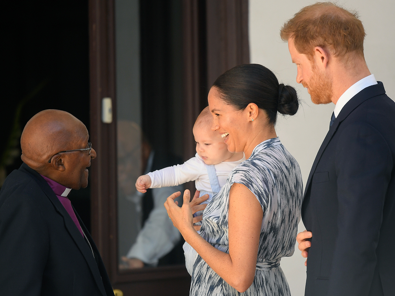 prince harry, meghan and archie with his arm outstretched to desmond tutu