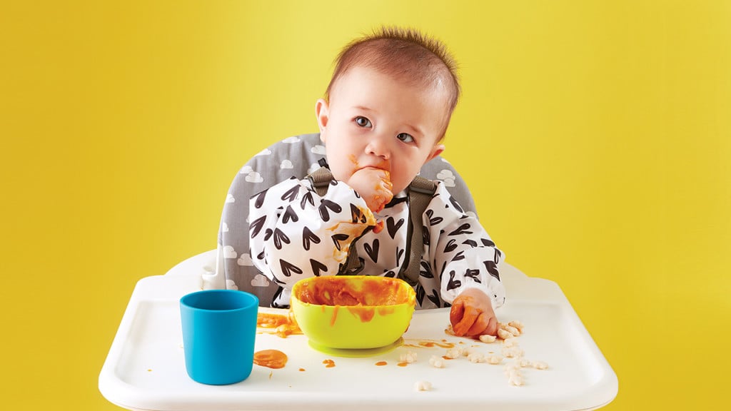 Baby self-feeding baby food in high chair