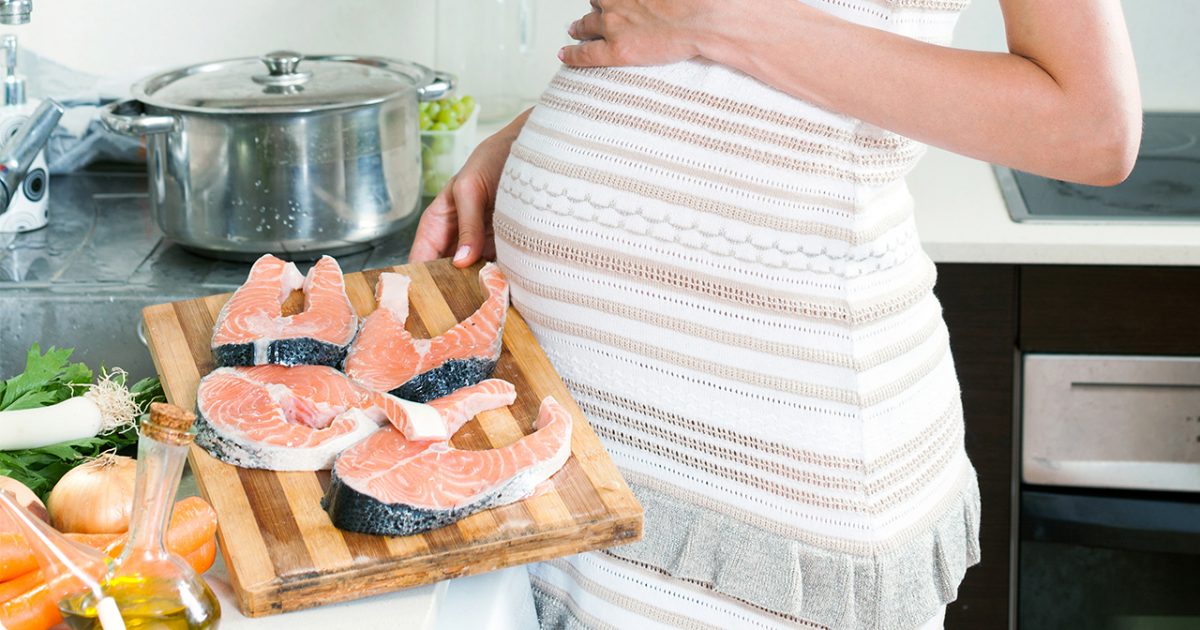 A pregnant woman shows off uncooked salmon.