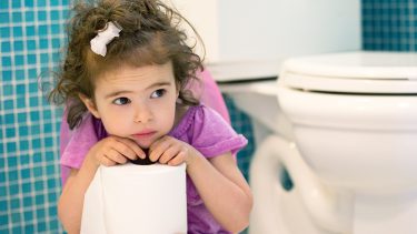 little girl sitting on toilet holding toilet paper