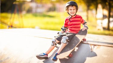 Boy sitting on a ramp with his skateboard, wearing a helmet and knee pads