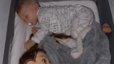 Baby sleeping while holding onto hair dressing mannequin