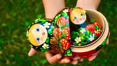 hands hold out Russian nesting doll over grass background