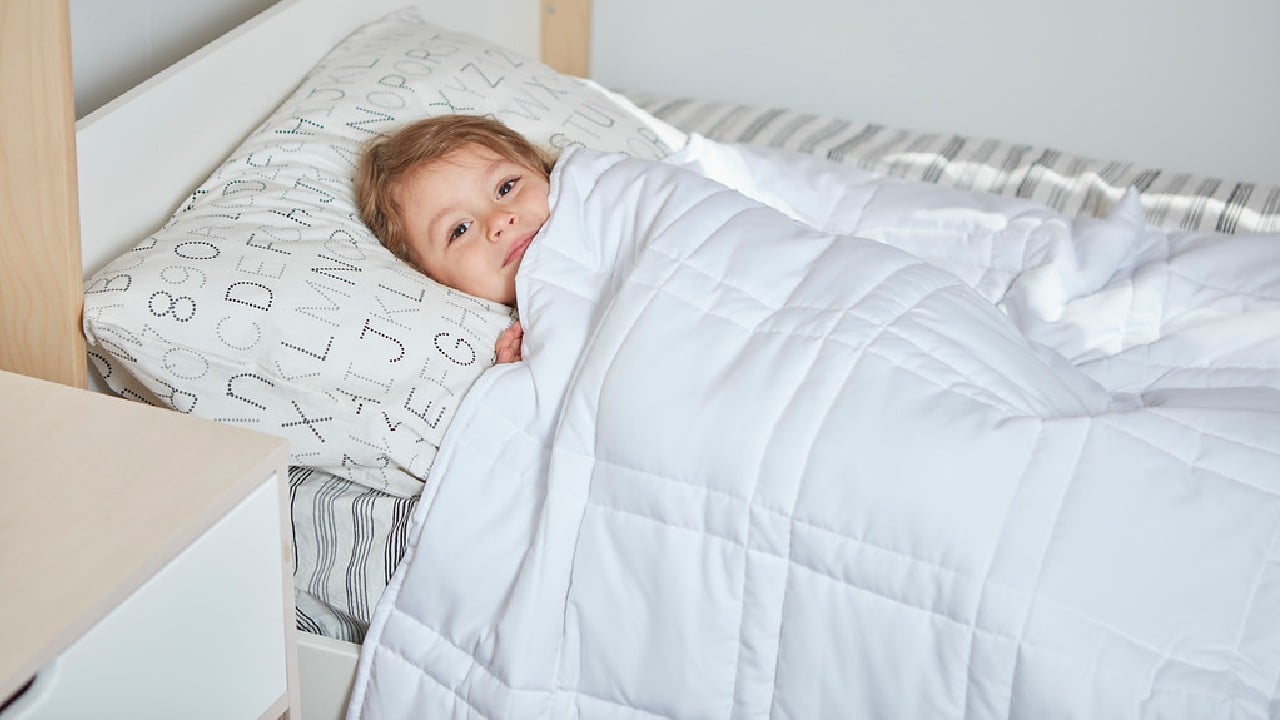 Kind im Bett unter einer gewichteten Decke
