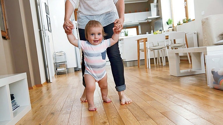 Photo of a baby starting to walk in the living room while being held up by an adult
