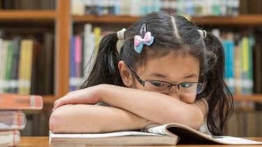 Child rests her arms on a book while looking sad, indicating dyslexia in children should be screened for.