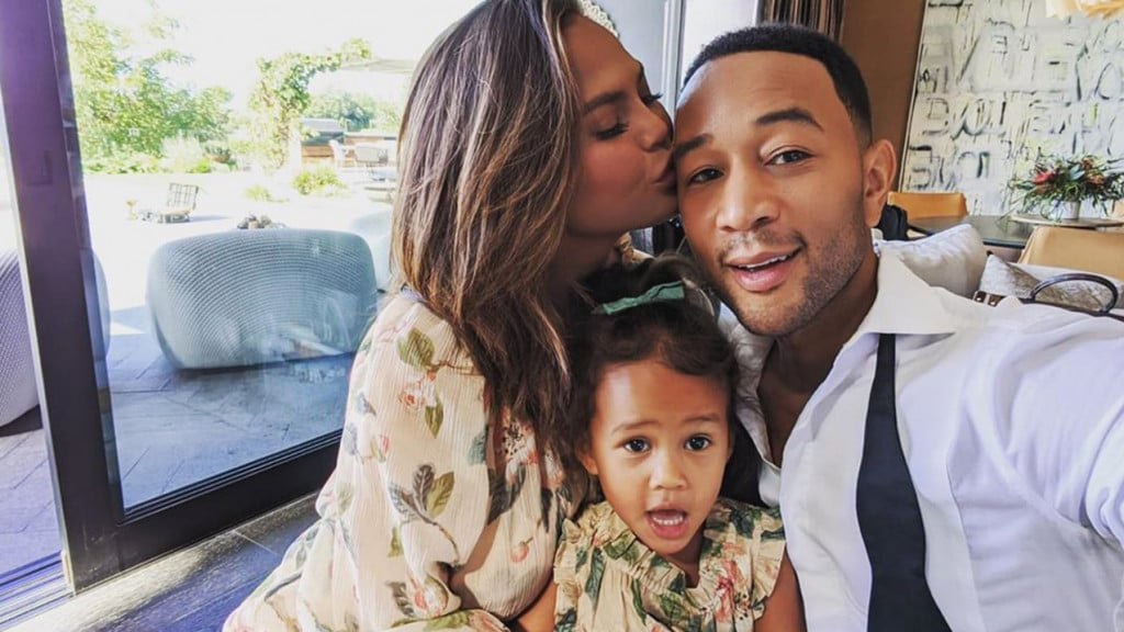 Chrissy kisses her husband on the head while they pose with their daughter Luna