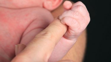 Newborn with possible erythema toxicum wraps hand around parent's finger