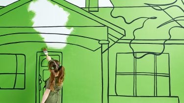 young girl painting a house green, symbolizing how to go green at home