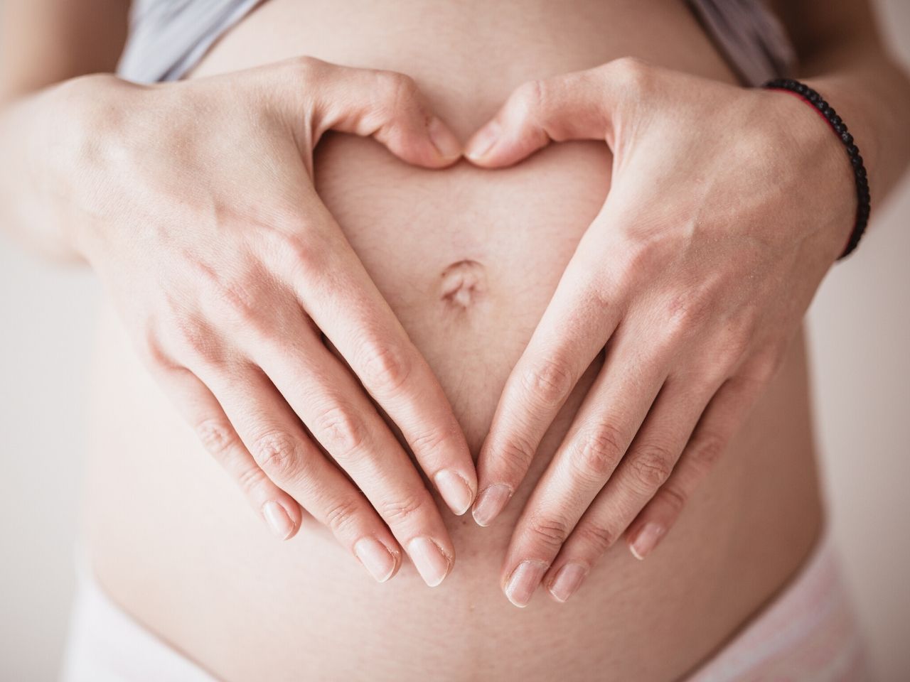 La mujer embarazada hace la forma de un corazón con sus manos y lo coloca en su vientre