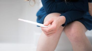 Woman holds pregnancy test while sitting down