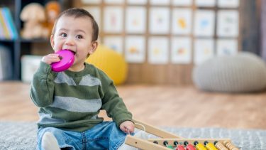 Best toys for 1 year old: Toddler puts wooden toy in his mouth