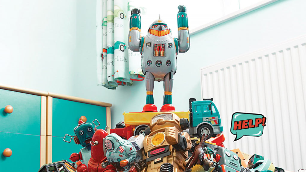 Toy robot standing on a pile of toys with his arms raised.