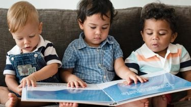 Three babies reading a book on the couch