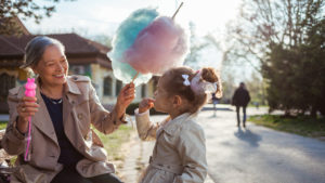 Grandma holds cotton candy and bubbles in her hands while granddaughter eats candy