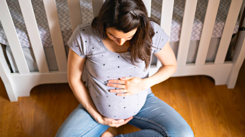 pregnant woman sitting on the floor of the nursery looking down at her baby bump