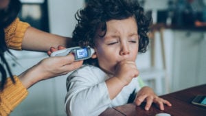 kid coughing while mom takes their temperature with an in-ear thermometer