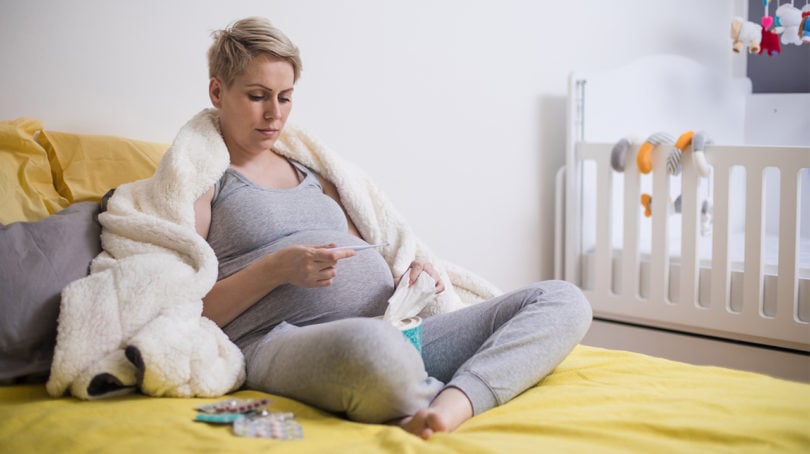 Pregnant woman sick in bed looking at a thermometer