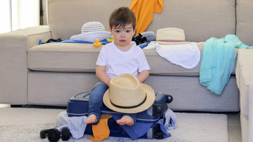 Little kid sitting on half packed suitcase waiting to leave for a trip
