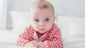 Creative baby names: A cute baby in a polka-dot pink jumper looks at the camera