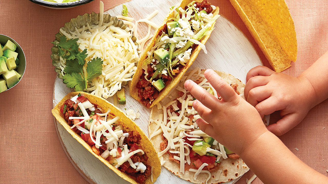 hands arranging cheese on tacos