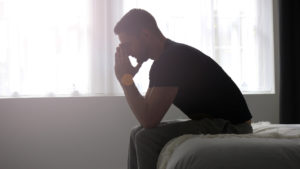 man looking upset while sitting on the edge of the bed
