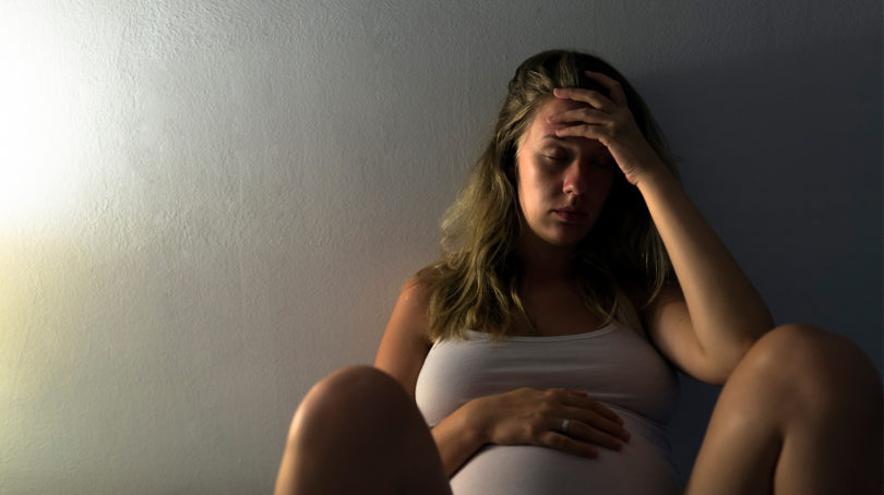 Giving birth during coronavirus: Pregnant woman looking worried while sitting up against a wall