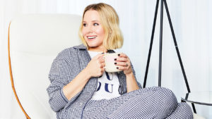 Kristen Bell sitting in pajamas on an armchair holding a mug