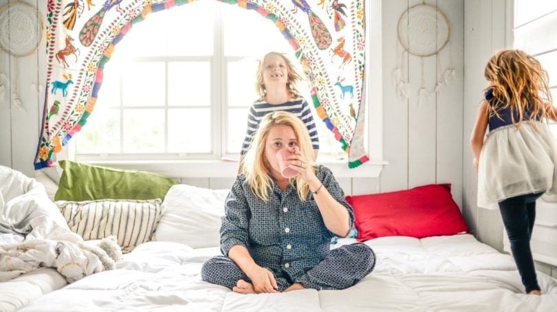 Parent guilt: A woman drinks coffee while her children jump on the bed