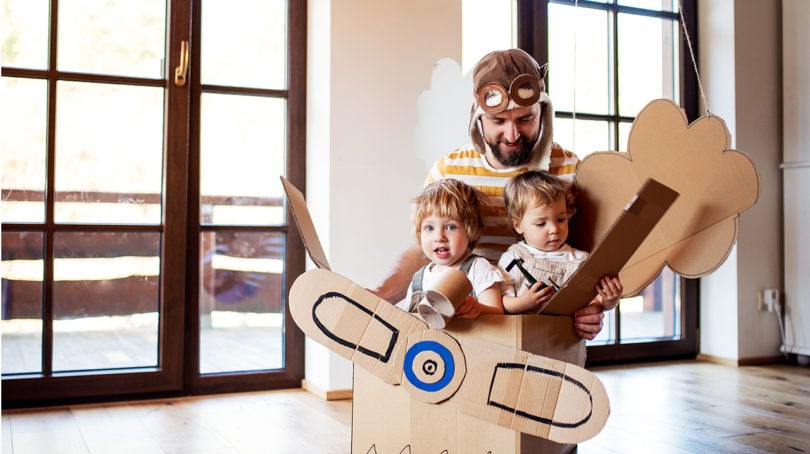 Father plays with his two children that pretend they are flying in a cardboard box.