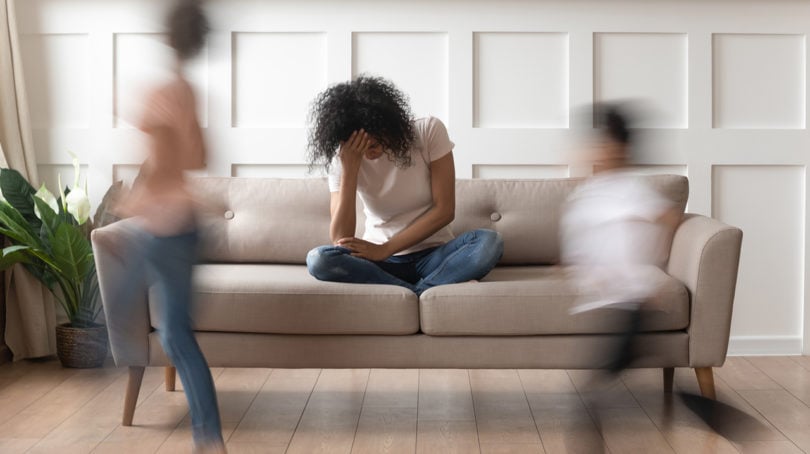 frustrated mom sitting on couch while her kids run around her