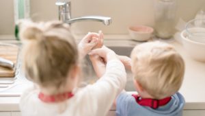 Siblings wash their hands together at kitchen sink