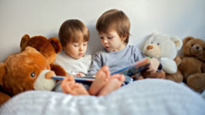 siblings reading a picture book surrounded by stuffed animals