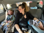 Mom sits in backseat of a car with newborn and older kid
