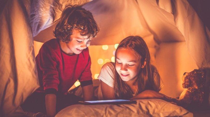 two kids looking at a tablet in a pillow fort