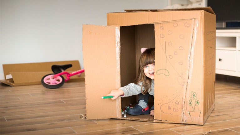 little kid playing in a cardboard box holding a marker