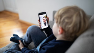 little kid sitting on a couch video chatting on a smartphone