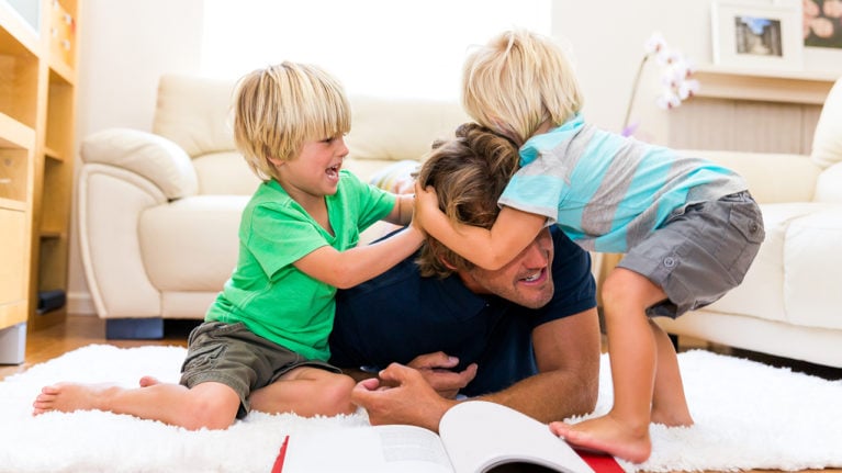 Kids roughhousing with dad on the living room floor